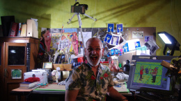 Friedel sits in his studio. Some of his artworks can be seen in the background.